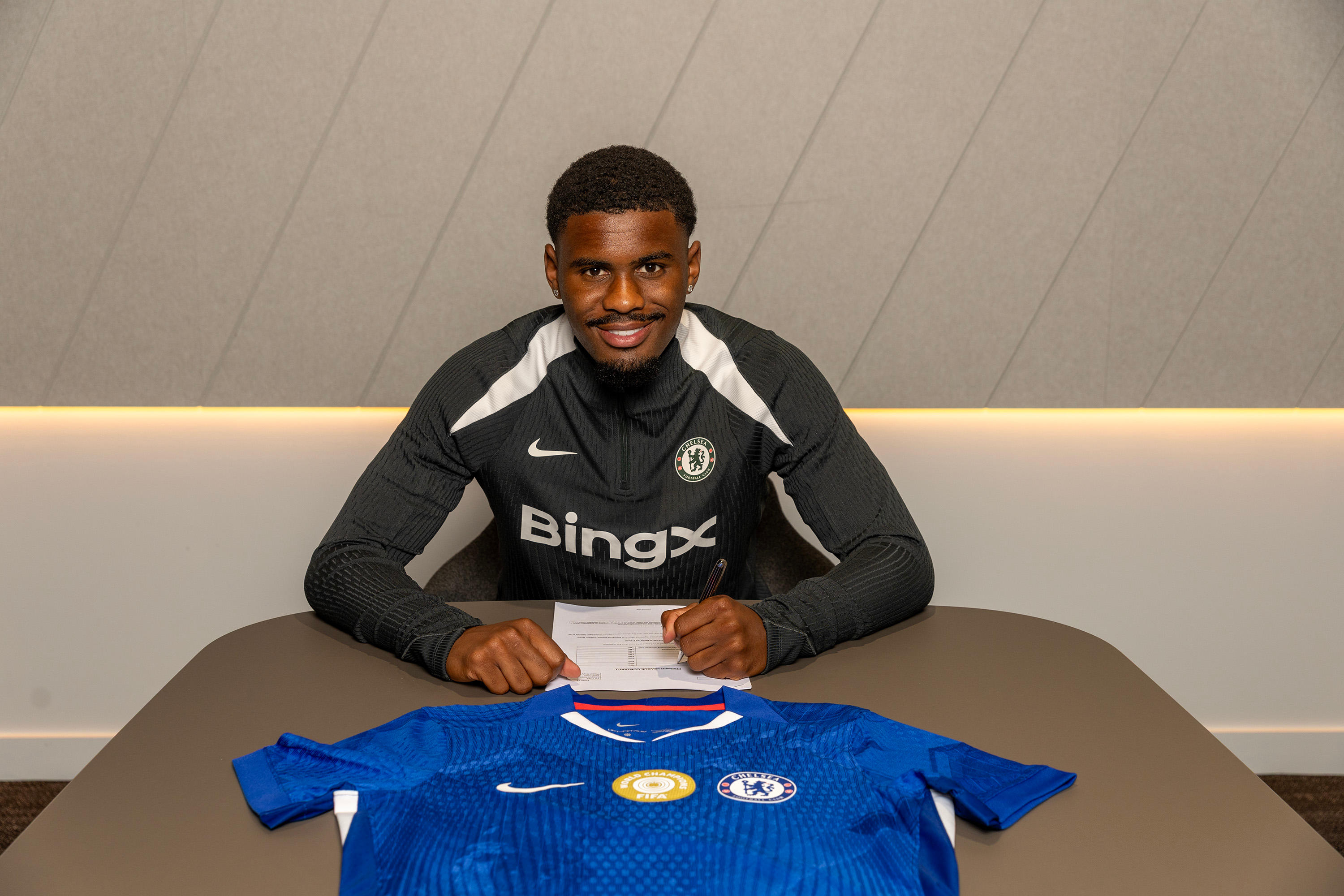 Jorrel Hato sits behind his Chelsea shirt while signing his contract
