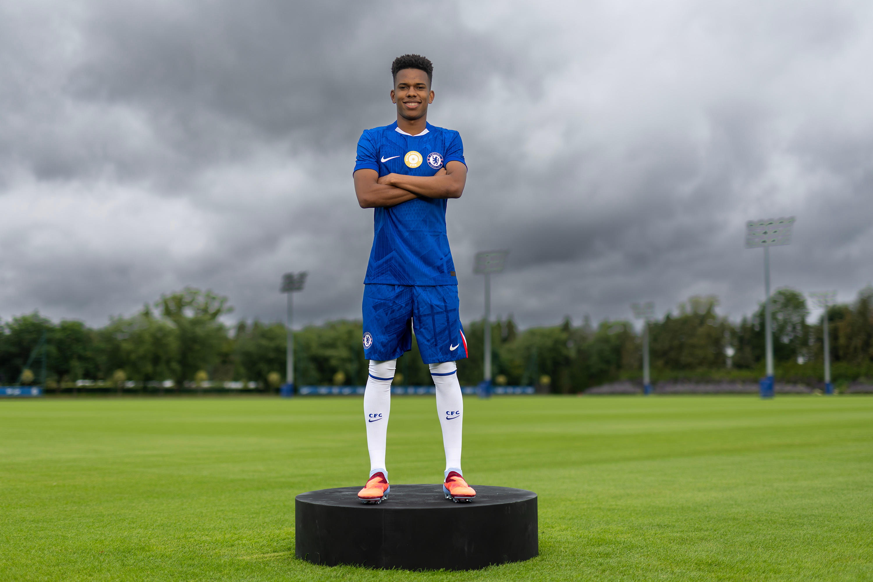 Estêvão stands on a plinth in full Chelsea kit on the Cobham pitch