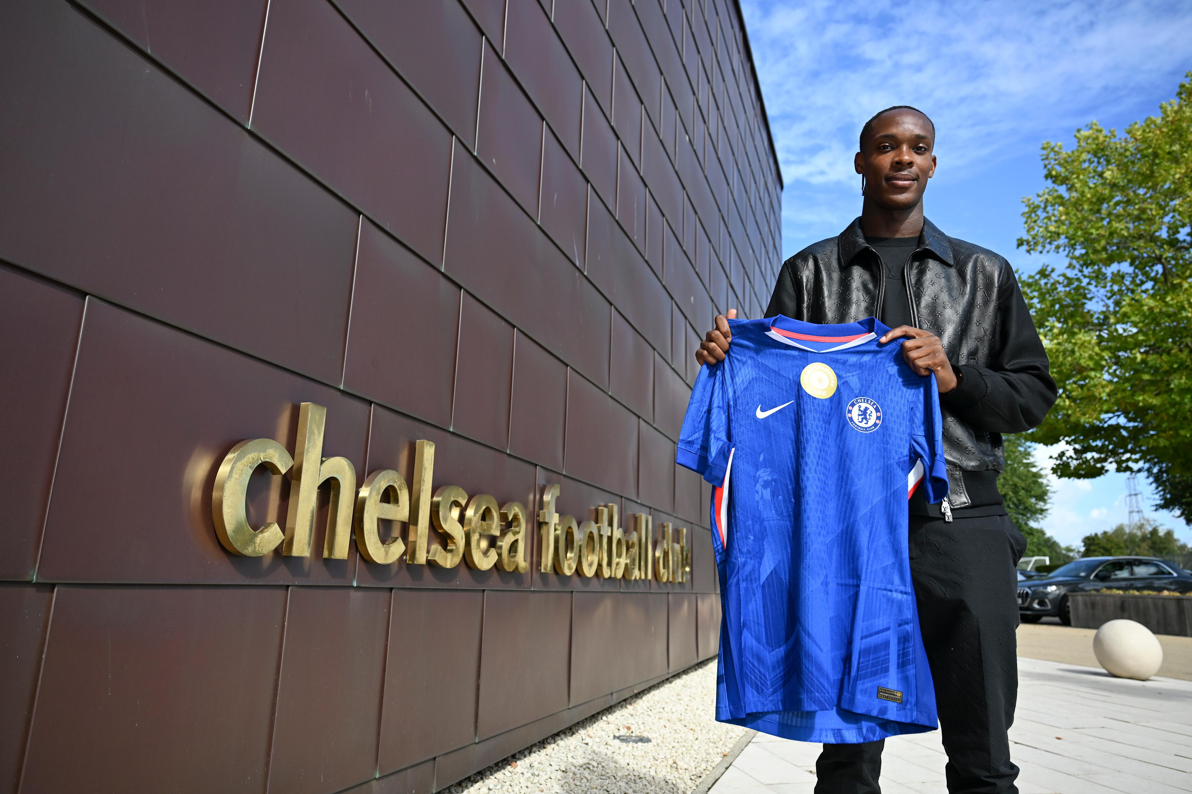 Emanuel Emegha holds a Chelsea shirt outside the club building at Cobham